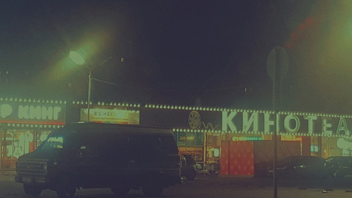 A dark van parked outside a cinema at night.