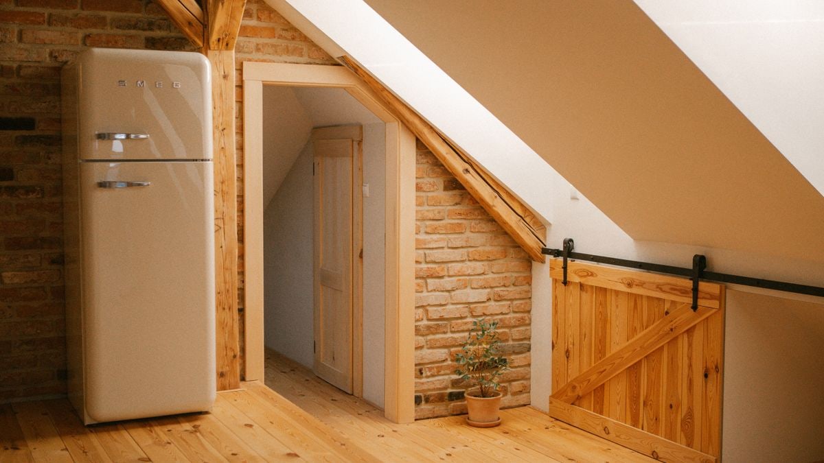 Rustic attic loft with wooden beams, vintage fridge, and warm ambiance.